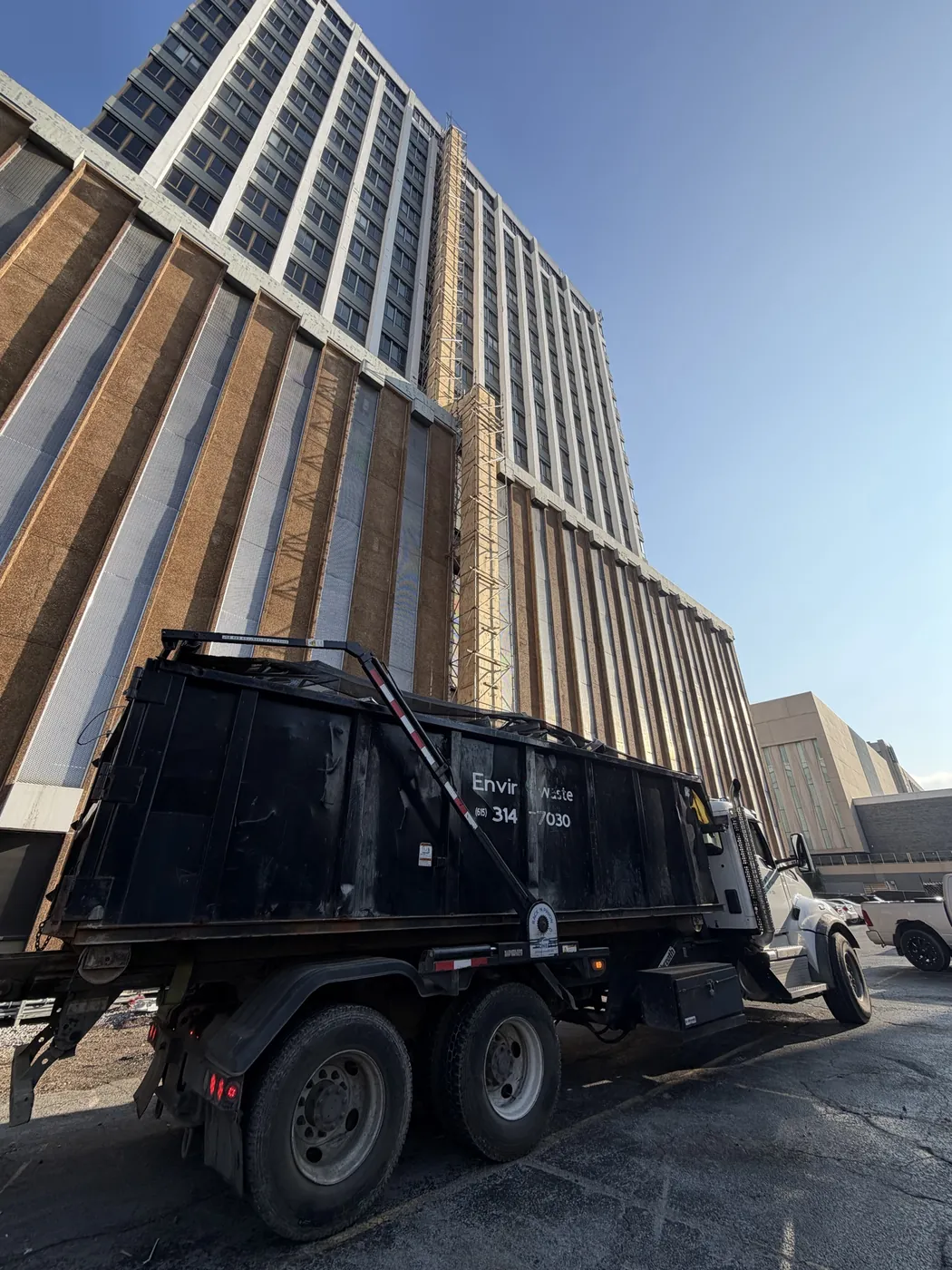 Waste disposal truck staged alongside a high-rise with exterior chute