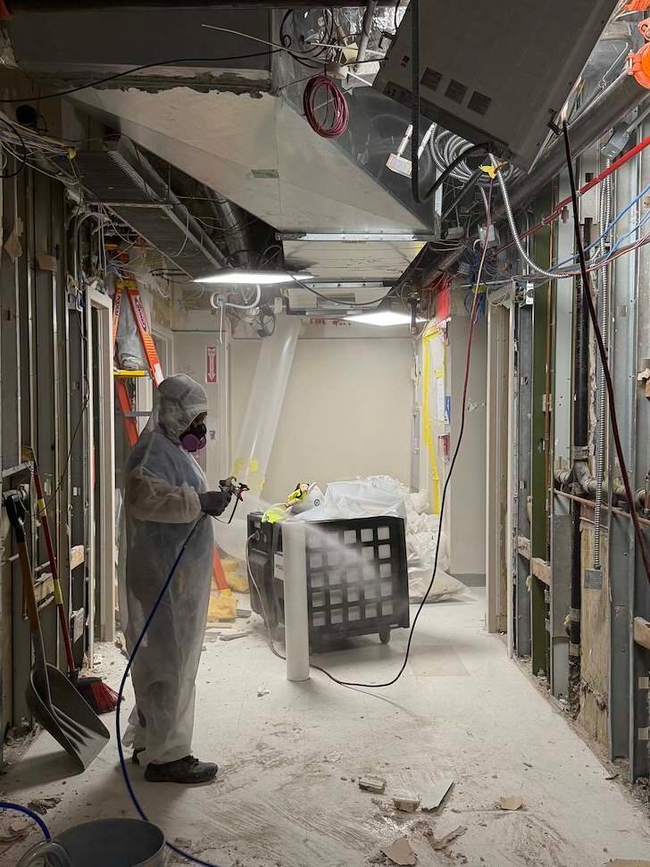 Asbestos abatement worker in full PPE spraying encapsulant